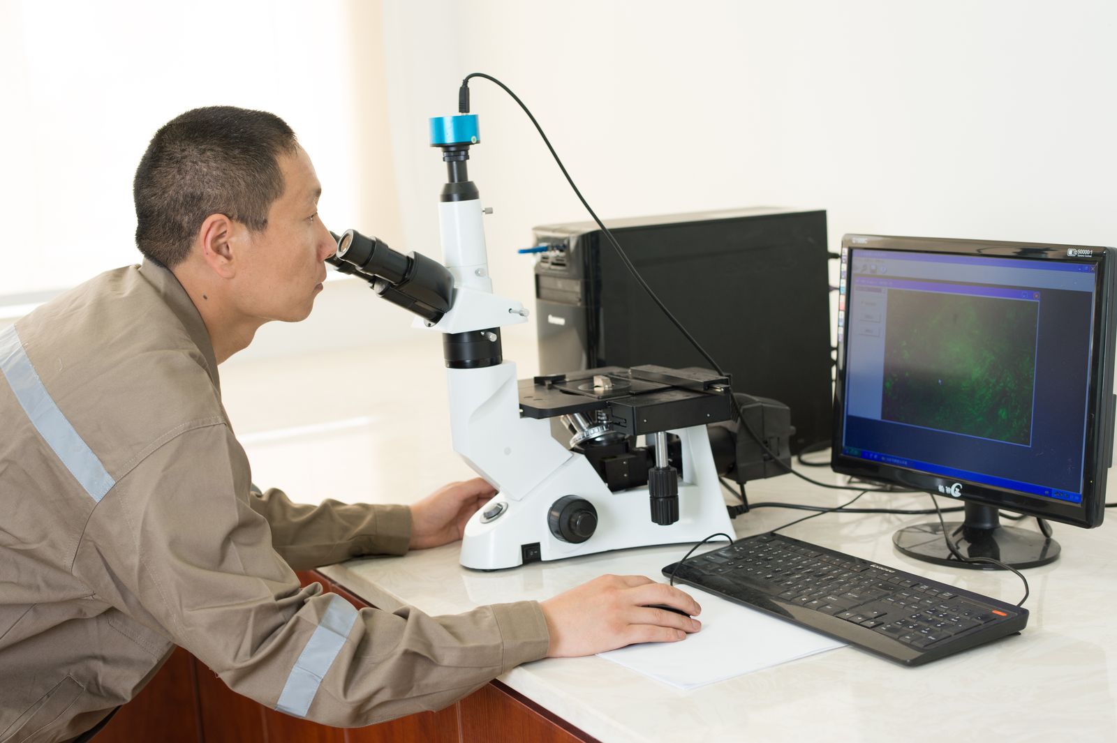 Técnico ao microscópio metalográfico, com a micrografia exibida no monitor