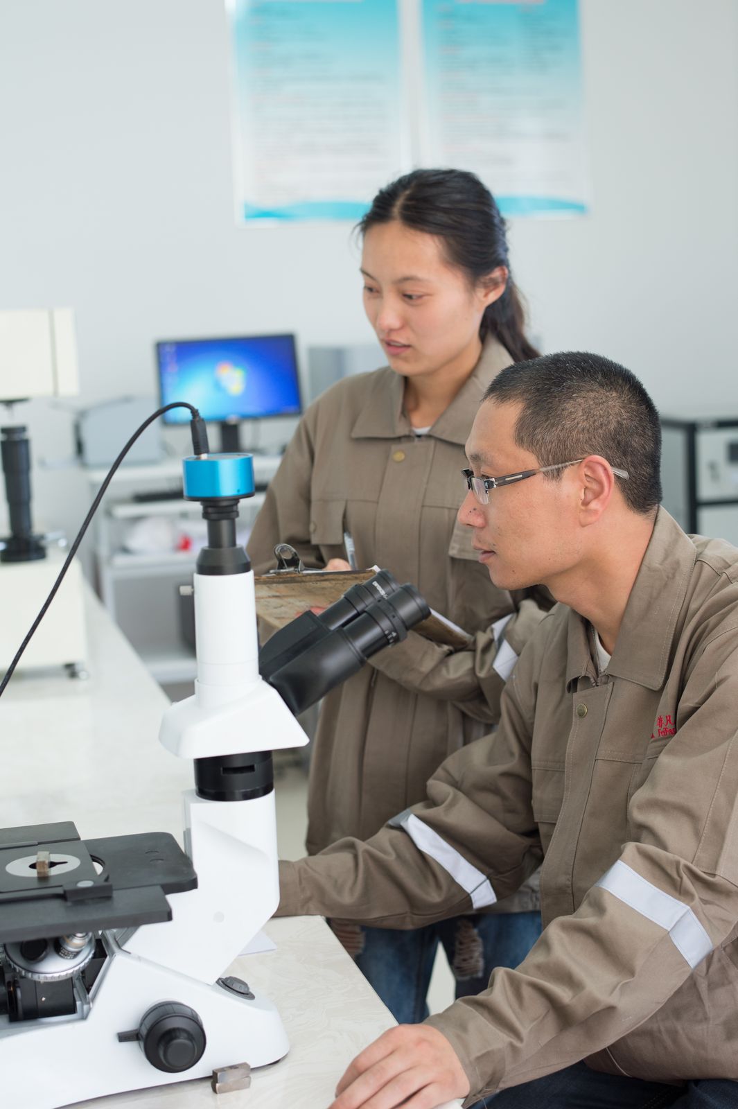 Dois técnicos analisando uma amostra ao microscópio e registrando os resultados