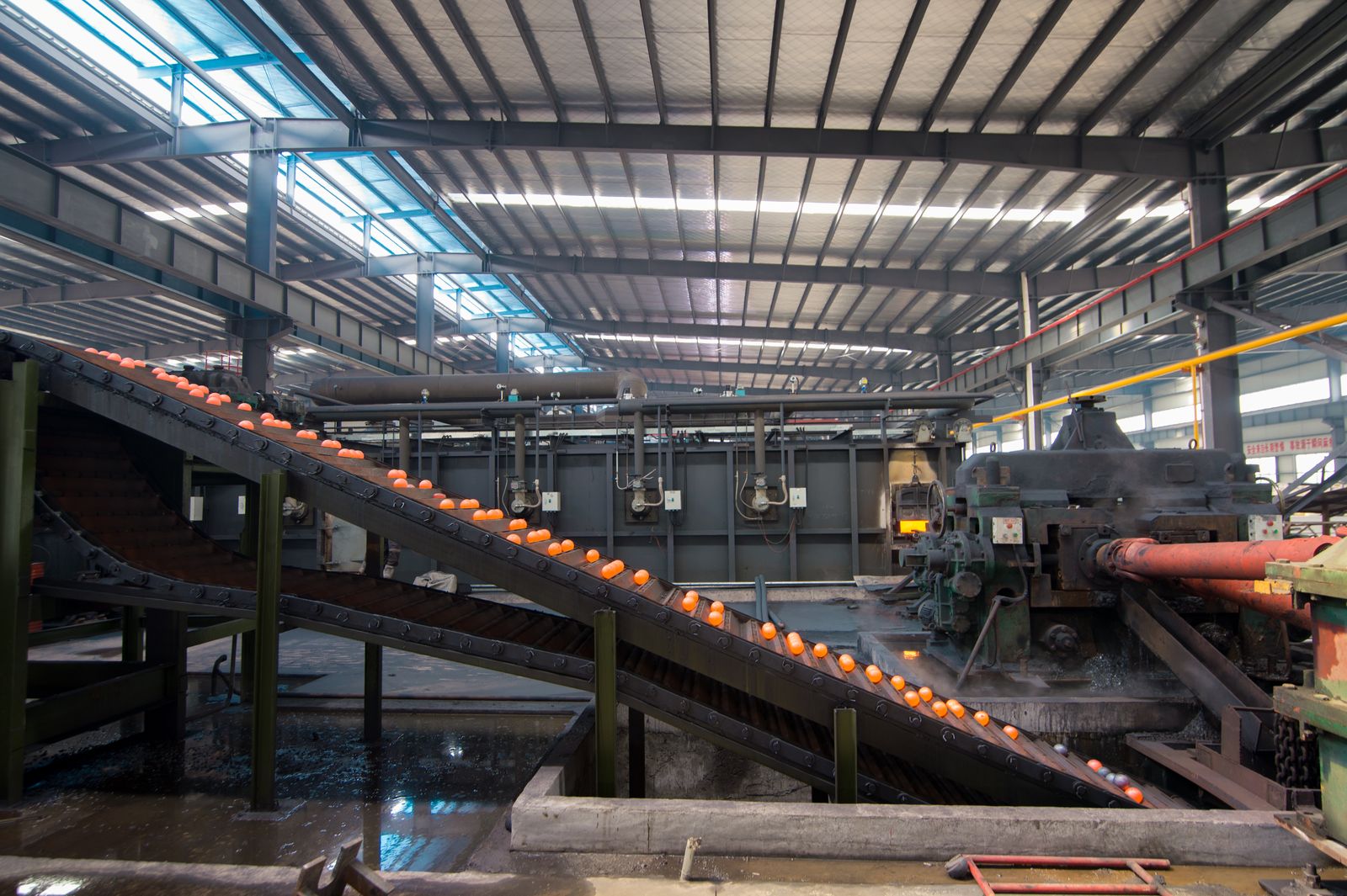 Vista interna da planta: transportador com bolas incandescentes ao lado do laminador e dos fornos